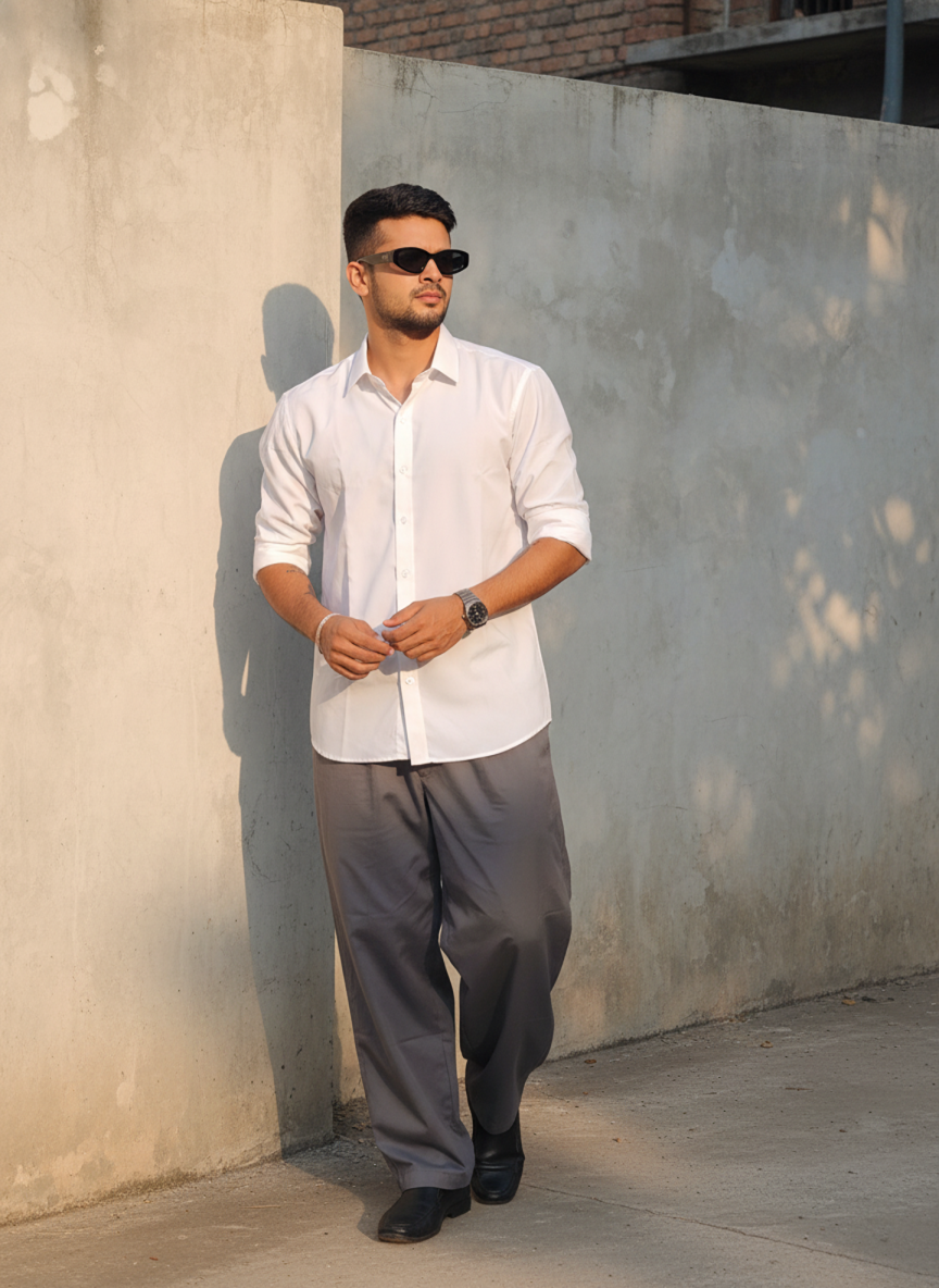 Man wearing a white shirt and gray pants standing against a concrete wall.